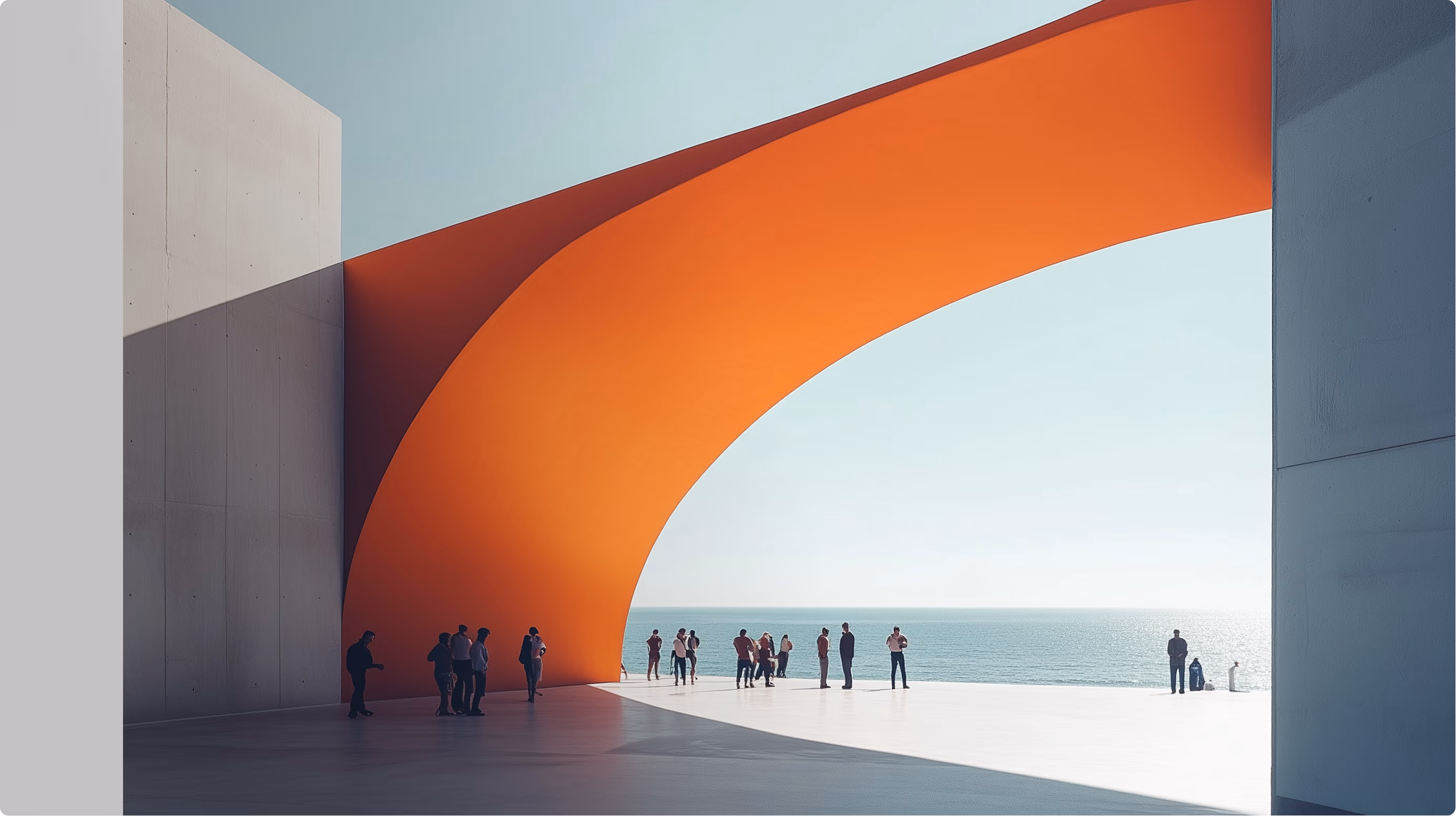 A man in a suit walks toward an outdoor seating area by a modern lakeside building with an orange overhang.